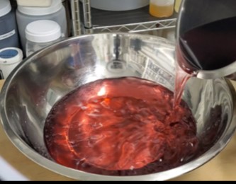 colored and fragranced wax for ice cream candles being poured into a stainless steel bowl