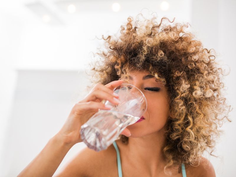 Woman drinking a glass of water representing Pillar 2 of the of the  7 pillars of holistic skincare, Proper Hydration.