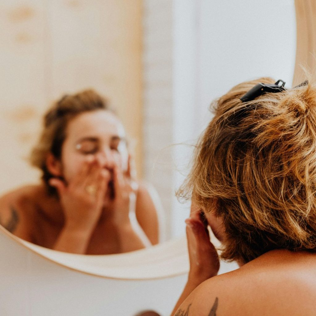 woman washing her face facing a mirror