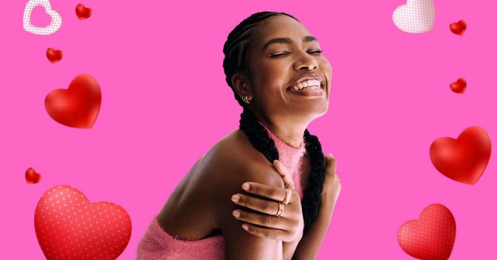 A joyful Black woman with braided hair smiles and hugs herself, surrounded by red and pink hearts on a bright pink background—symbolizing self-love and emotional warmth for February.